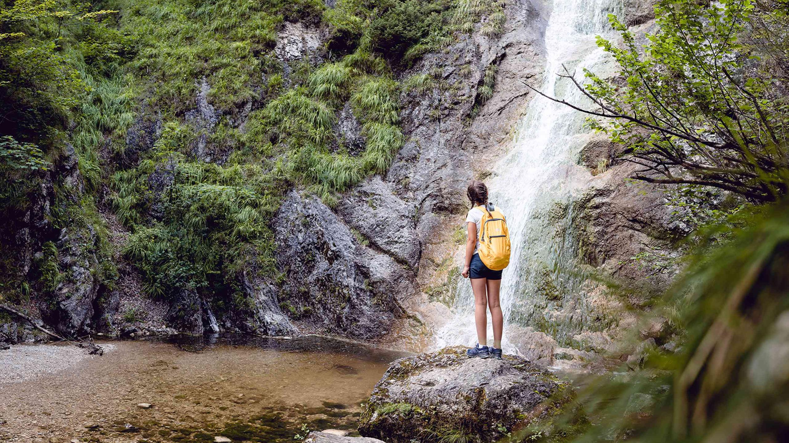 Vor einem Wasserfall steht eine Frau auf einem Felsen