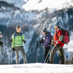 In Winterlandschaft ist ein Ranger mit drei Erwachsenen auf Schneeschuhen unterwegs