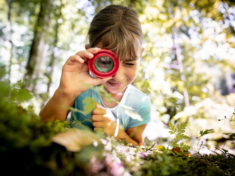 Ein Mädchen beobachtet durch ein Lupenglas den Waldboden