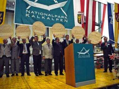 Politiker und Gemeindevertreter stehen auf Bühne und halten eine Holzscheibe mit Nationalpark Kalkalpen Logo hoch