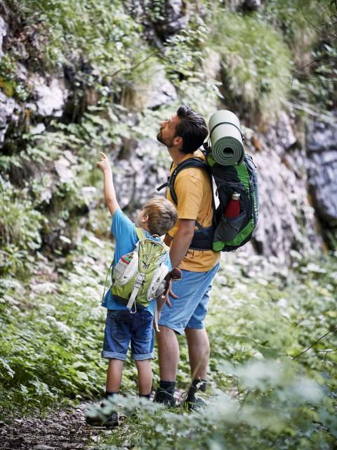 Vater und Sohn stehen auf Wanderweg und schauen an einem Felsen hoch
