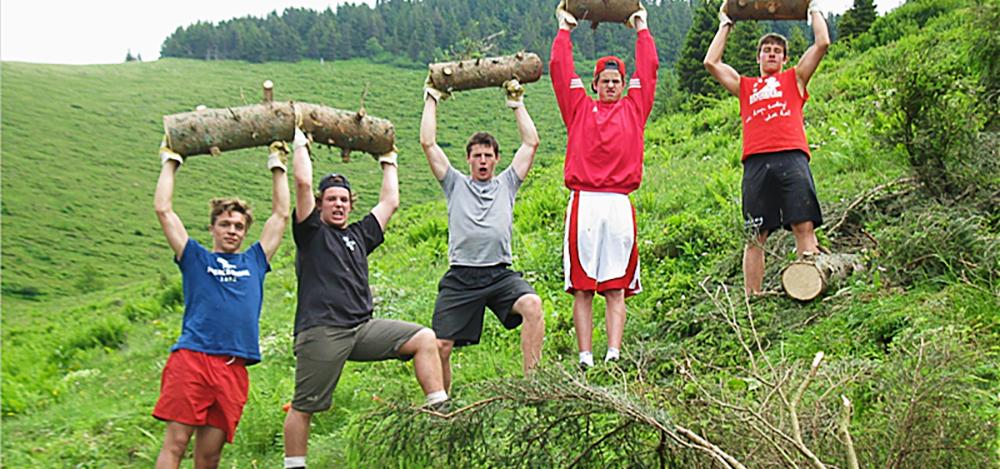 Fünf Burschen halten triumphierend je ein Stück von einem Fichtenbaumstamm über dem Kopf