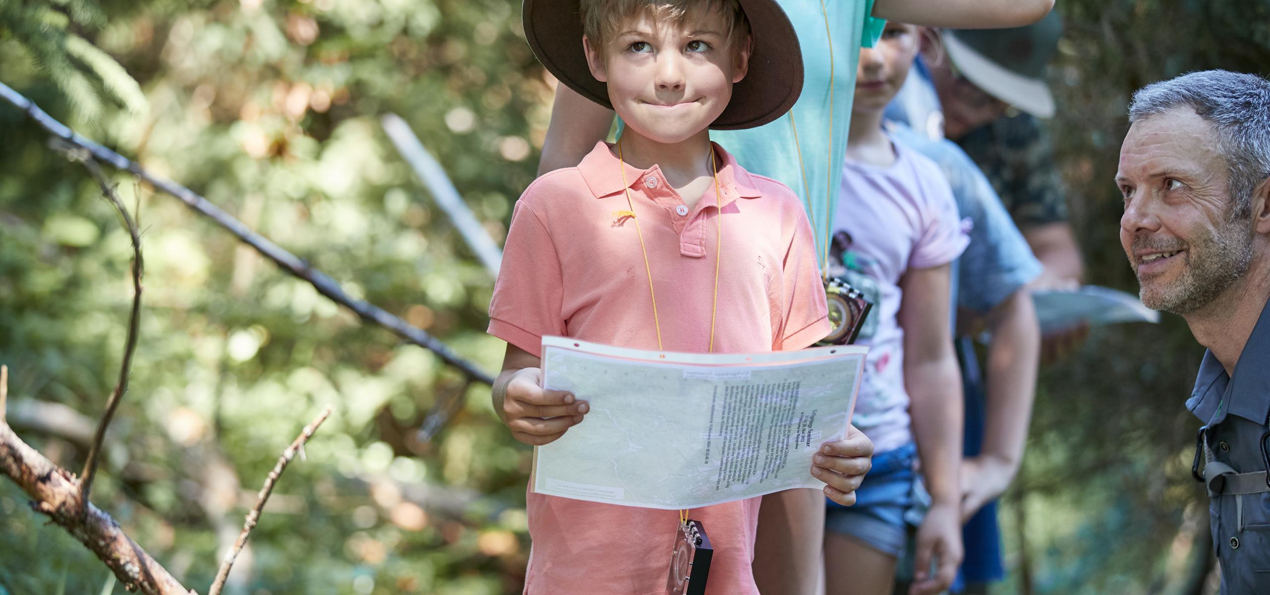 Ein kleiner Junge versucht sich im Wald mit Kompass und Plan zu orientieren