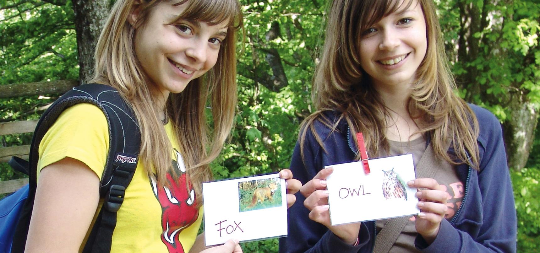 Zwei Mädchen halten englisch beschriftete Tierkärtchen in Händen