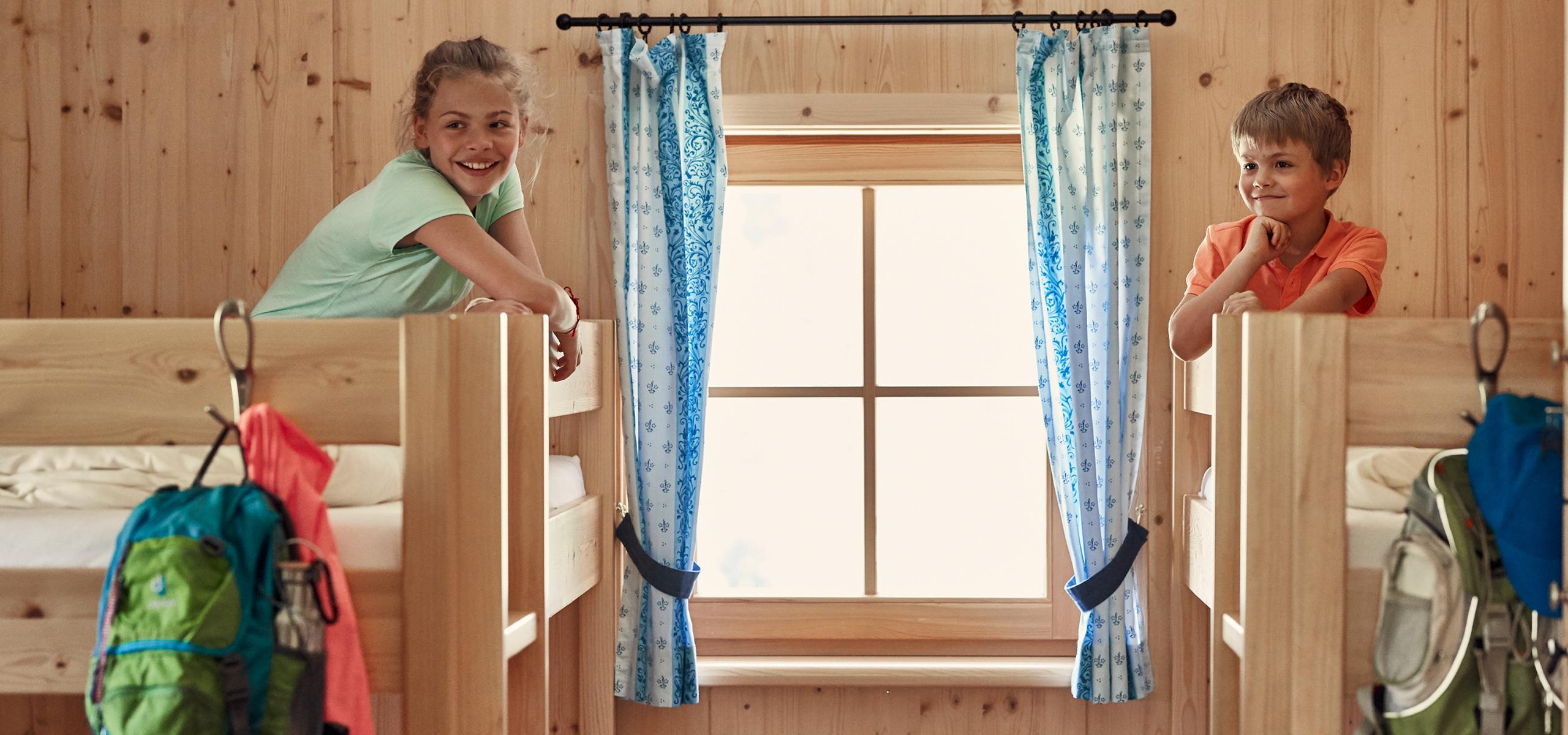 Zwei Kinder sitzen in Stockbetten in einem mit Holz vertäfelten Zimmern