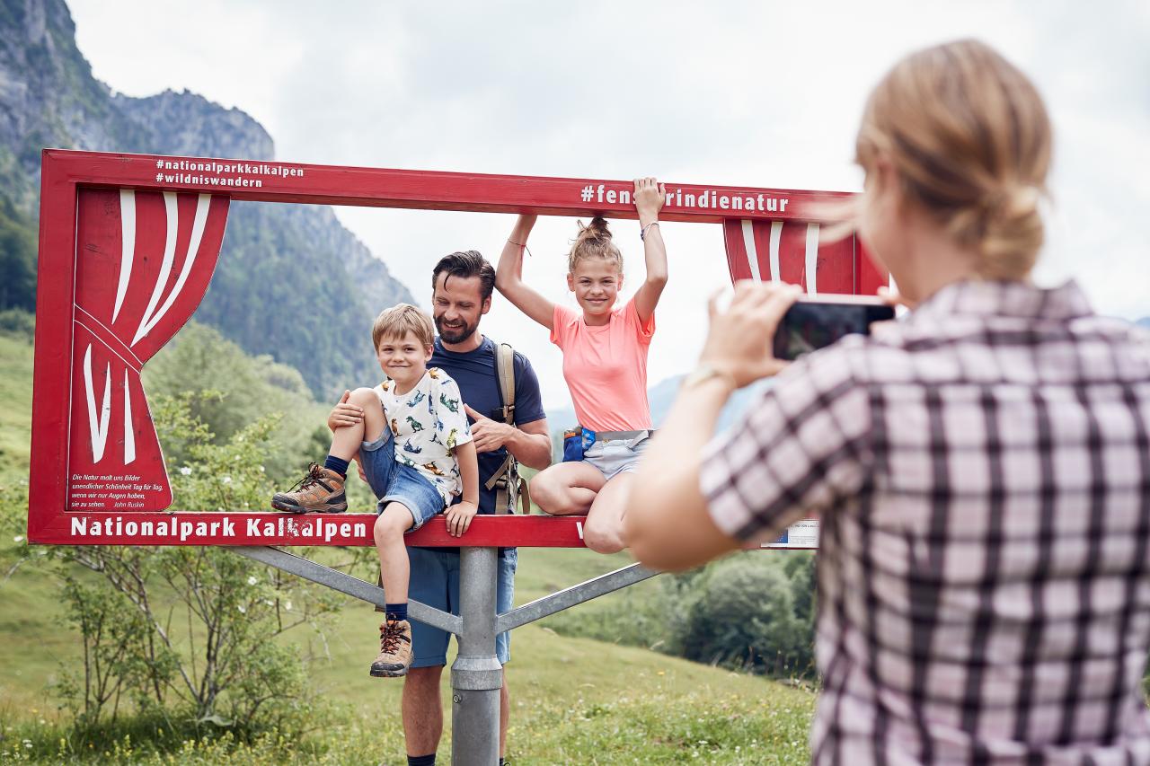 Frau fotografiert einen Mann und zwei Kinder in einem Selfie Fotorahmen auf Almwiese