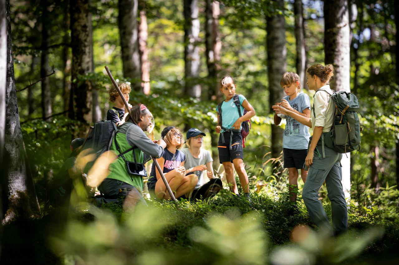 Nationalpark Rangerin und Ranger unterhalten sich mit einer Gruppe Kinder im Wald