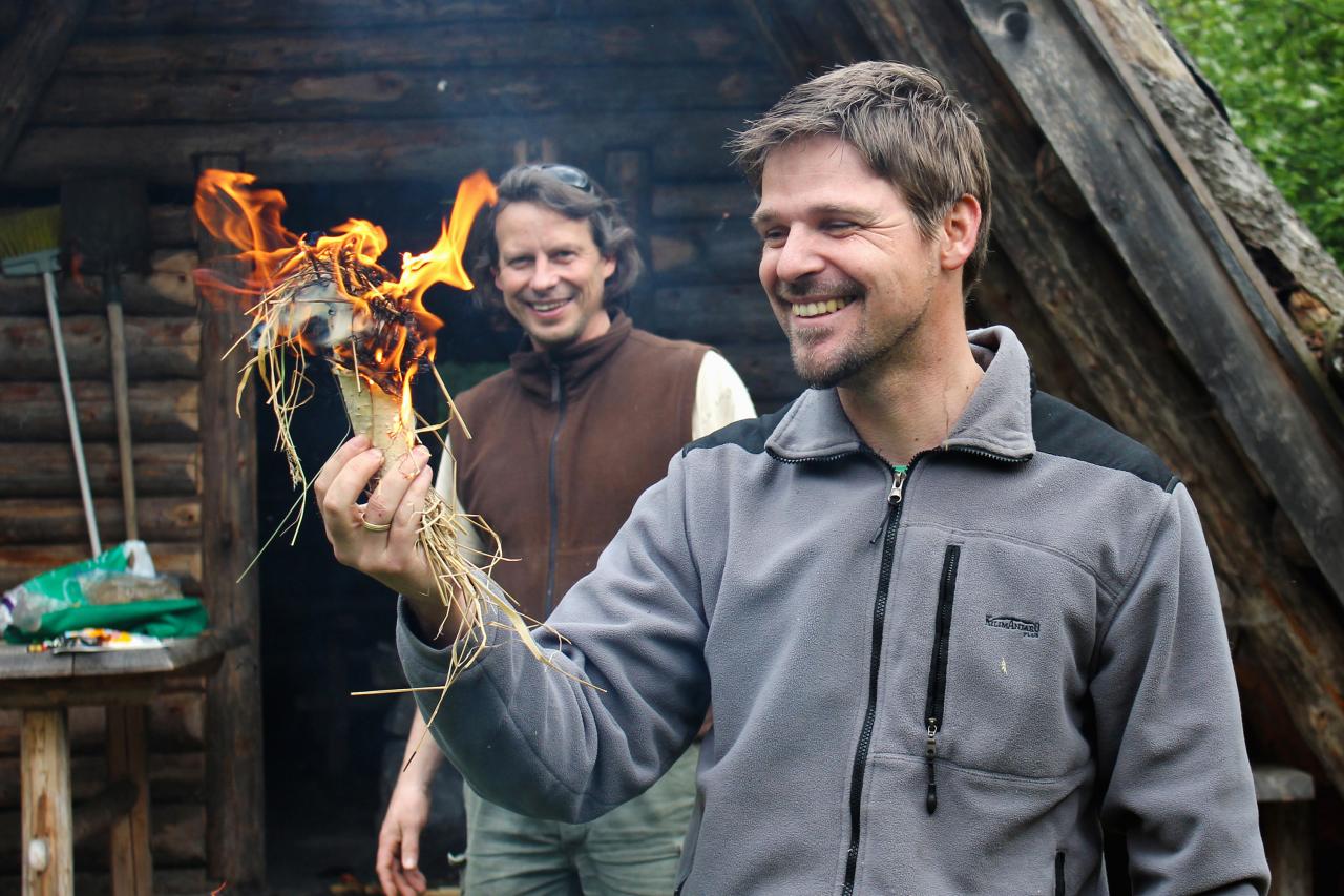 Zwei Männer entzünden Feuer in einem mit Gras befüllten Stück Birkenrinde