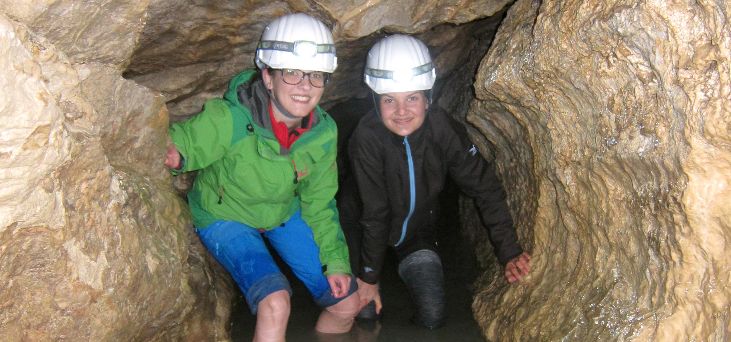 Zwei Kinder waten in einem Höhlengang knietief durchs Wasser