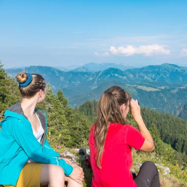 Zwei Frauen sitzen auf Berggipfel und schauen über Bergpanorama