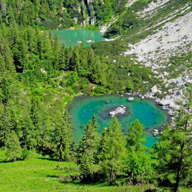Zwischen steil abfallendem Geröllfeld und Bergwald liegen zwei kleine smaragdgrüne Seen