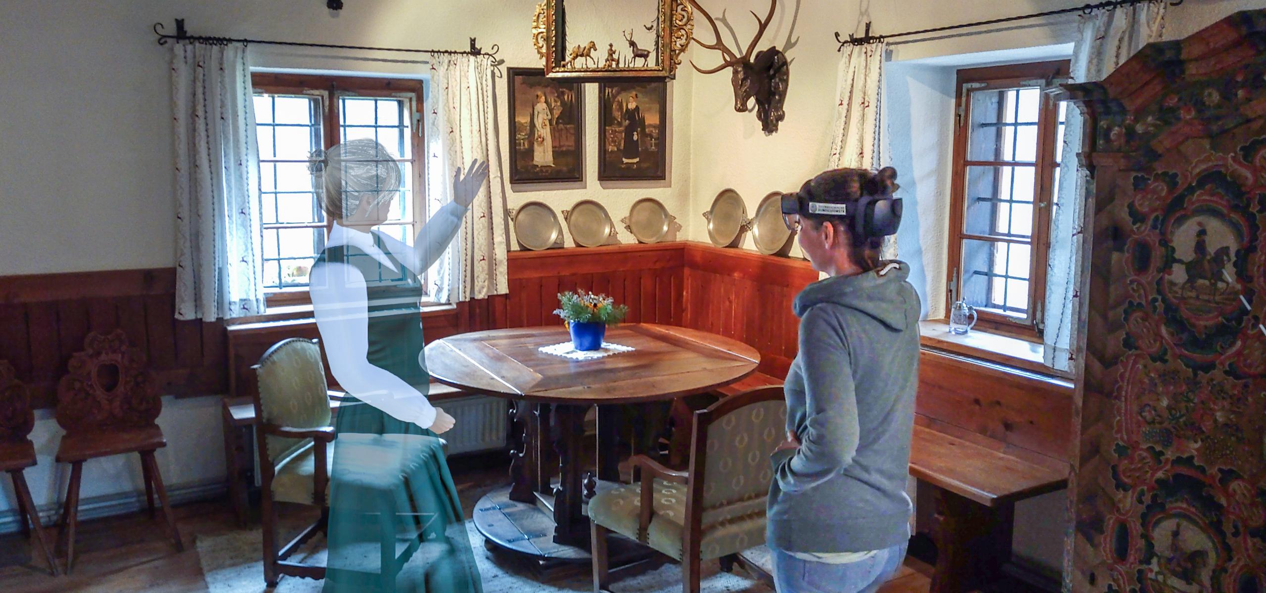 Die virtuelle Anna von Lamberg zeigt einer Besucherin bei einer Augmented Reality Tour im Forsthaus Bodinggraben auf eine Rothirsch Trophäe.