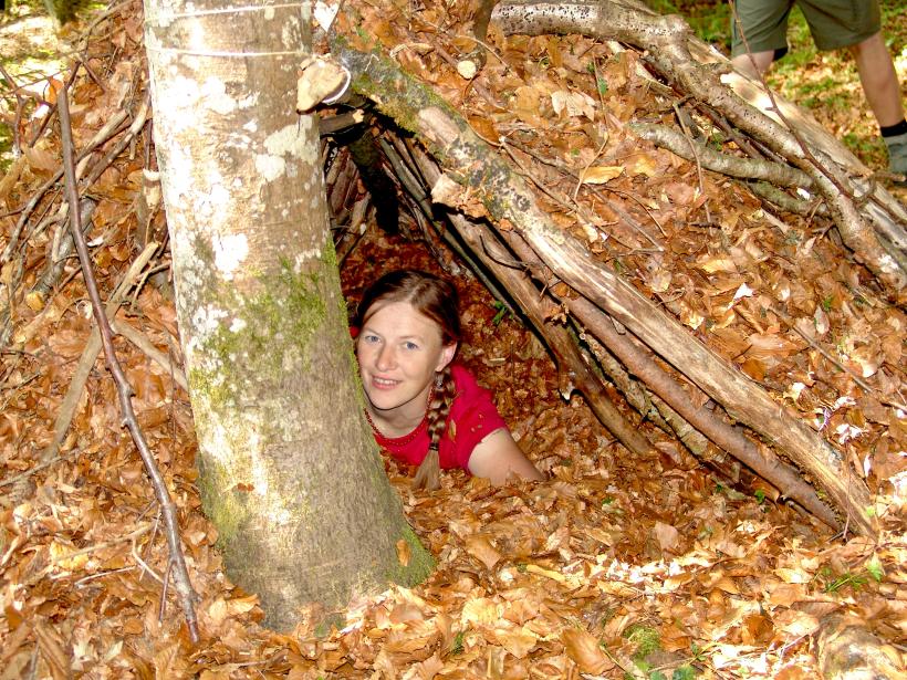 Eine Frau hat sich in ein aus Ästen und Laub gebautes Duck zurückgezogen