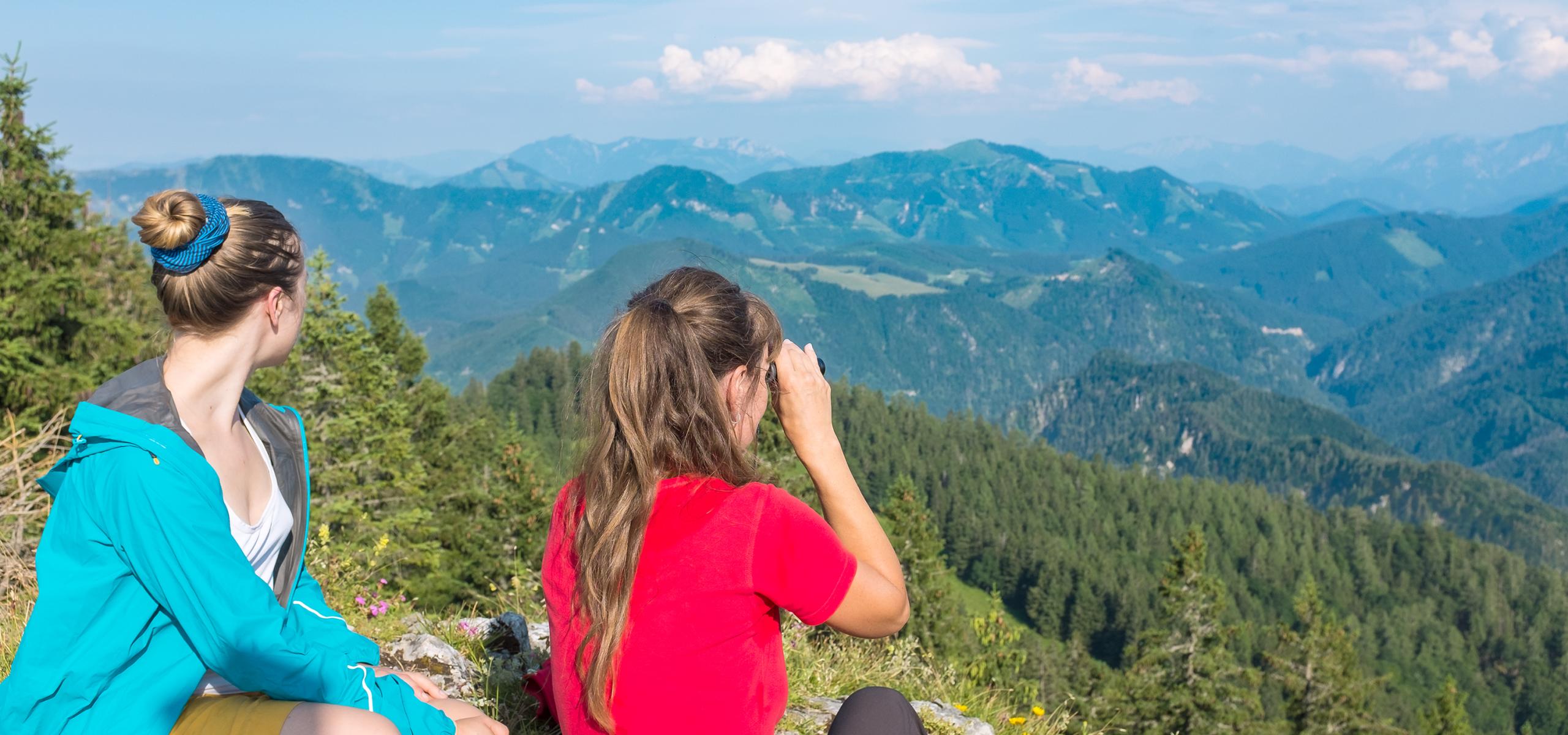 Zwei Frauen sitzen auf Berggipfel und schauen über Bergpanorama