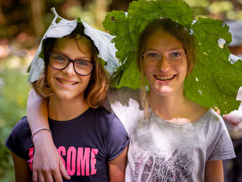 Zwei Mädchen haben ein großes Huflattich Blatt auf den Kopf aufgesetzt