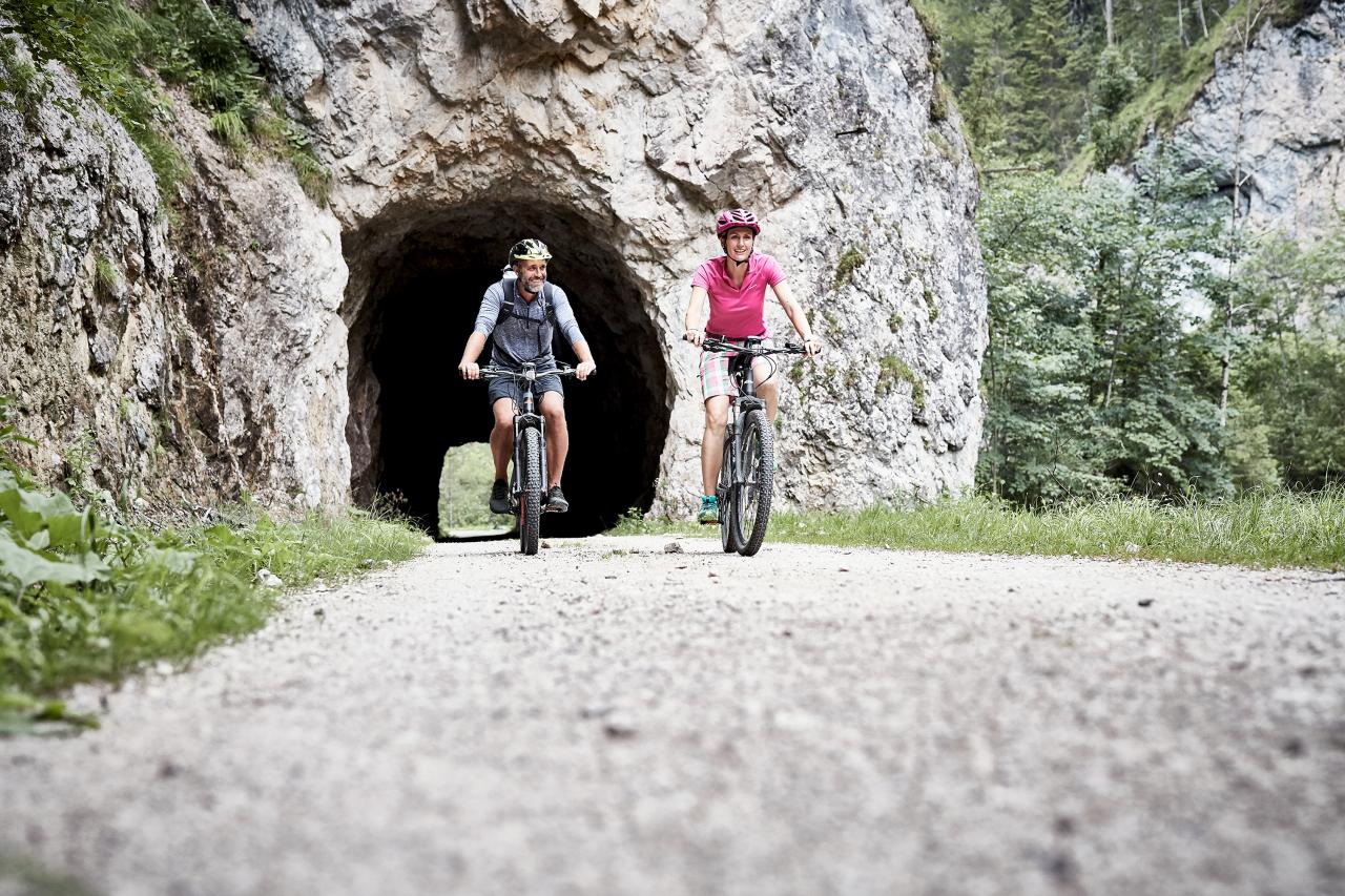 Eine Frau und ein Mann fahren mit ihrem Mountainbikes aus einem Felstunnel heraus