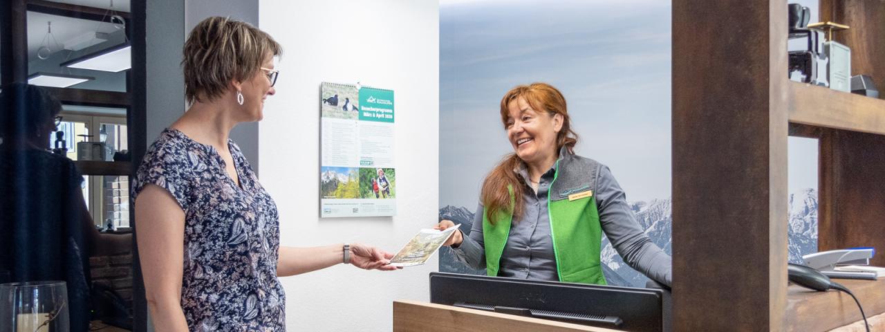 An einem Infopult spricht eine Nationalpark Mitarbeiterin mit einer Besucherin